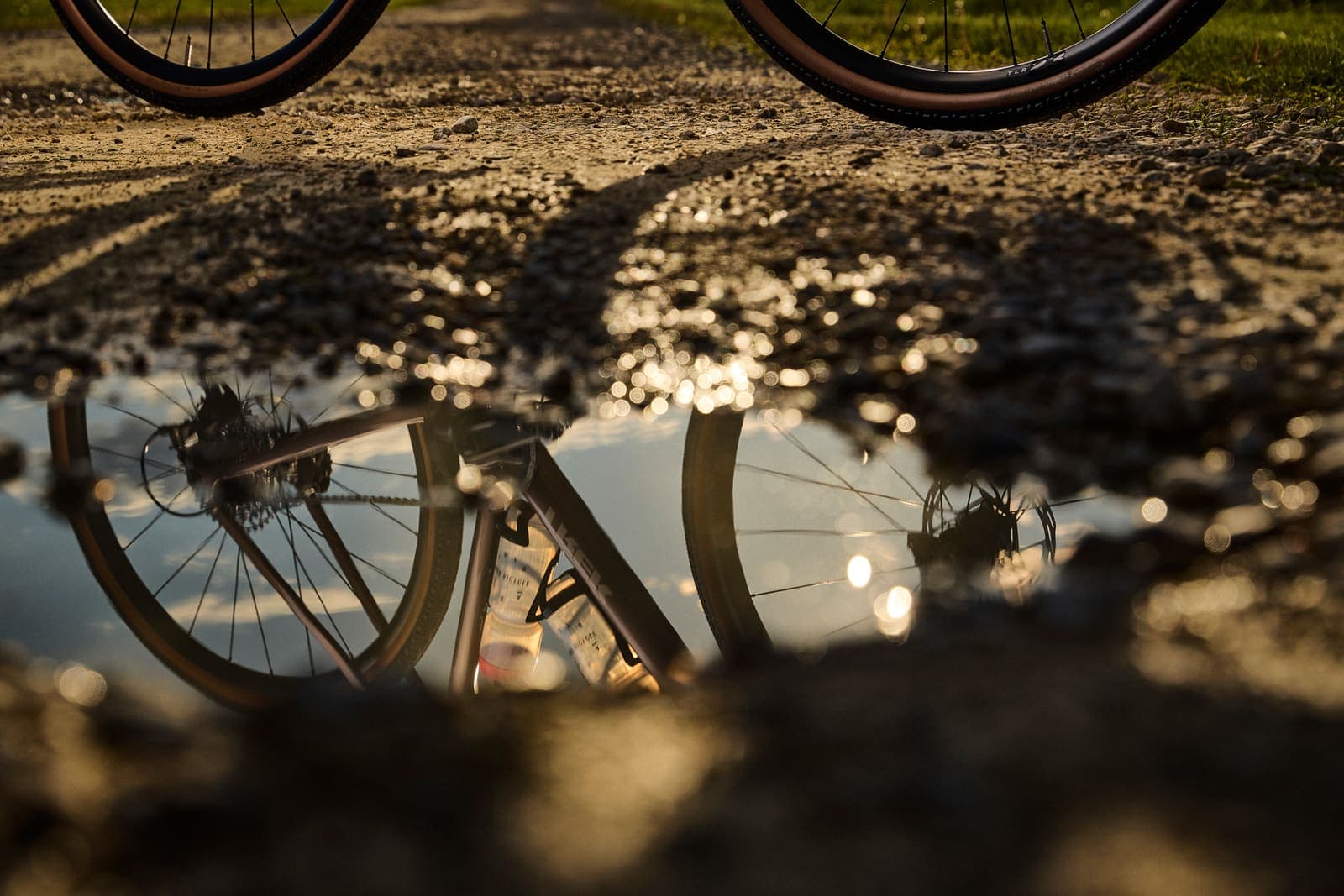Gravel bicikl zrcali se u lokvi na makadamu u zlatnom satu